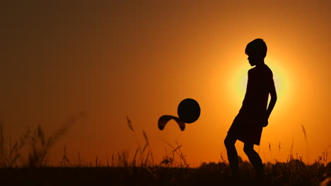 Silhouette-Eines-Jungen,-Der-Am-Strand-Football-Oder-Fußball-Spielt,-Mit-Wunderschönem-Sonnenuntergang-Im-Hintergrund,-Sportliches-Lifestyle-Konzept-Für-Die-Gelassenheit-Der-Kindheit.